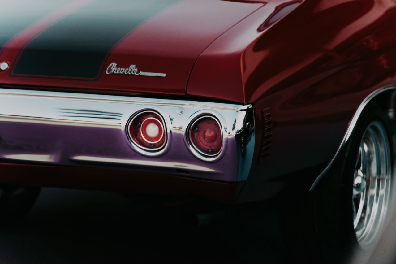 creative-02 Detailed shot of a vintage red Chevrolet muscle car's rear with chrome detailing.