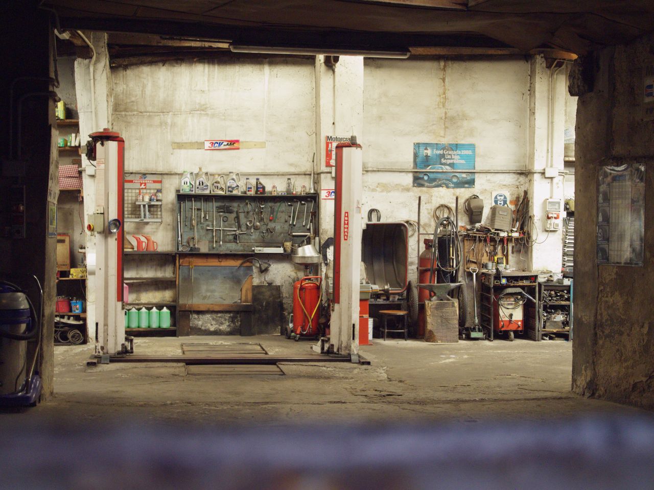 digital An empty, rustic car workshop featuring tools, machinery, and car lifts in an industrial setting.