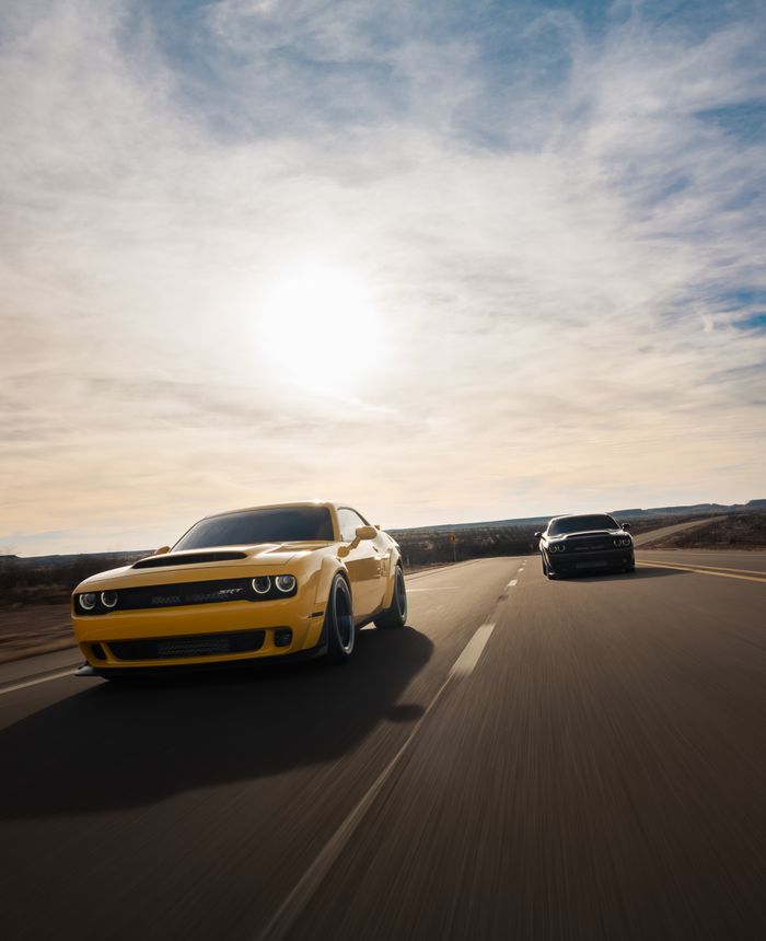 creative-01 Two powerful muscle cars racing on an open highway under a bright sun, showcasing speed and adrenaline.