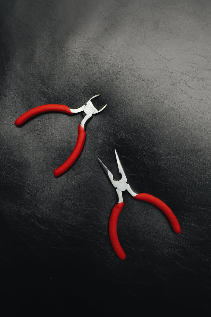 creative-02 Two red handled pliers on a dark leather texture for crafting or repair work insight.